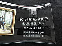 「医科大学のマーク 祝副院長御就任 ○○先生」を彫刻した副院長就任祝い用の名入れ写真立て