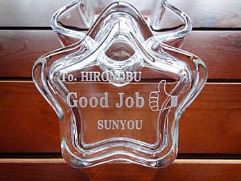 「永年勤続者の名前、サムアップのイラスト、会社名」を蓋に彫刻した、永年勤続の表彰記念品用のガラス製小物入れ