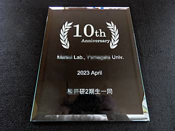 「10th anniversary ○○Lab.○○Univ. 2023April ○○研2期生一同」を彫刻した、大学の研究室の周年祝い用のガラス盾