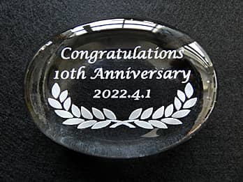 「Congratulations 10th Anniversary、日付」を彫刻した、会社の10周年記念品用のガラス製ペーパーウェイト