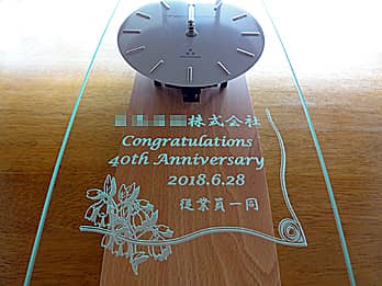 「会社名、お祝いメッセージ、周年を迎える日付、贈り主の名前」を前面ガラスに彫刻した、周年祝い用の掛け時計