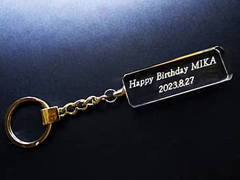 「Happy Birthday、贈る相手の名前、誕生日の日付」をガラス製の飾り部に彫刻した、誕生日プレゼント用のキーホルダー
