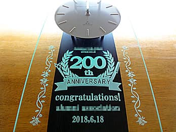 「お客さまがデザインしたオリジナル図案」を前面ガラスに彫刻した、周年祝い用の掛け時計