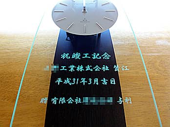 「祝竣工記念 ○○株式会社賛江 有限会社○○与利」を彫刻した、竣工祝い用の掛け時計