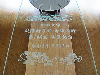 「○○大学 健康科学部看護学科 第一期生 卒業記念」を前面ガラスに彫刻した、卒業生から学校へ寄贈する掛け時計