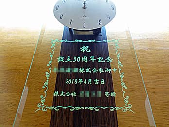 「お祝いメッセージ、贈り先の会社名、贈り主の会社名」を前面ガラスに彫刻した、周年祝い用の掛け時計