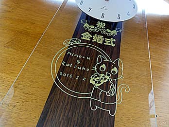「祝金婚式、両親の名前、猫のイラスト」を前面ガラスに彫刻した、両親の金婚式祝い用の掛け時計