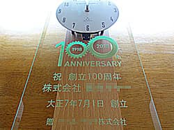 「祝創立100周年、株式会社○○、贈○○株式会社」を前面ガラスに彫刻した、お取引先へ贈呈する創立100周年祝い用の掛け時計