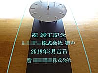「祝竣工記念、○○株式会社御中、贈 株式会社○○」を彫刻した、お得意先への竣工祝い用の掛け時計
