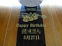 「趣味サークルのマーク、Happy Birthday、贈る相手の名前、誕生日の日付」を前面ガラスに彫刻した、誕生日プレゼント用の振り子時計