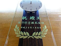 「祝竣工、○○株式会社、日付」を前面ガラスに彫刻した、竣工祝い用の掛け時計