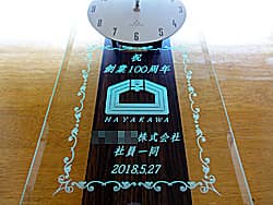 「祝 創業100周年、○○株式会社社員一同より、会社のロゴマーク」を前面ガラスに彫刻した、創業100周年祝い用の掛け時計