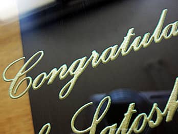 就任祝い用の掛け時計の前面ガラスに彫刻したお祝いメッセージ（Congratulations）を、ゴールドに着色加工した彫刻部のクローズアップ画像