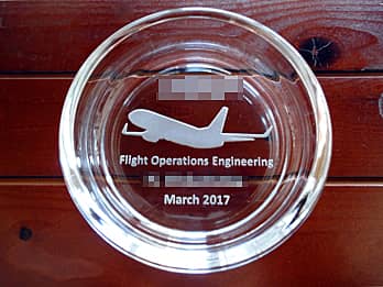 「ロゴマーク、飛行機のイラスト、部署名、永年勤続者の名前」を底面に彫刻した、永年勤続表彰用のガラス製灰皿