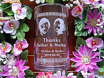 新郎と新婦の似顔絵を、側面に彫刻した円柱形のフラワーベース（新郎と新婦から両親への贈呈品）