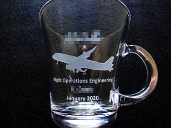 「会社のロゴマーク、飛行機のイラスト、退職する方の名前」を側面に彫刻した、定年退職祝い用のガラス製ティーカップ