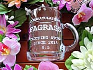 「Congratulations、店名とキャッチフレーズ」を側面に彫刻した、開店祝い用のガラス製マグカップ