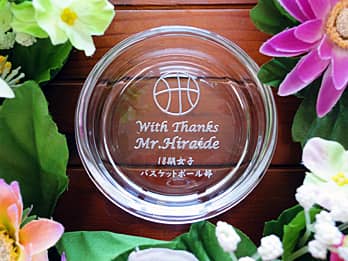 「バスケットボールのイラスト、感謝を込めたメッセージ、先生の名前、贈り主の名前」を底面に彫刻した、卒業生から部活の先生へのプレゼント用のガラス製灰皿
