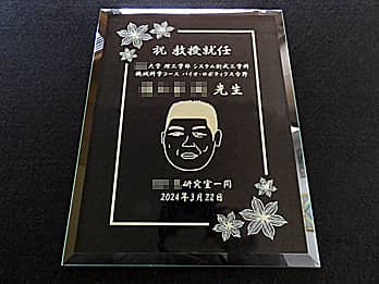 教授の似顔絵を彫刻した教授就任祝い用のガラス盾