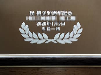 「祝創立50周年記念 株式会社○○ 社員一同より」を表面に彫刻した、周年祝い用のインテリアミラー