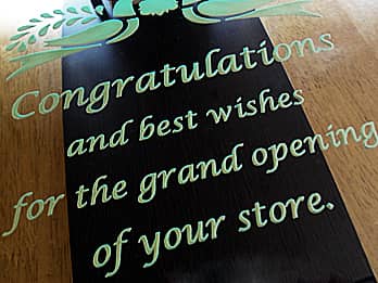 ゴールドに着色した、開店祝い用の掛け時計の前面ガラス部に彫刻した「Congratulations and best wishes for the grand opening of your store」のクローズアップ画像