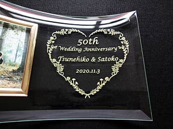「50th Wedding Anniversary、旦那様と奥さまの名前、結婚記念日の日付」を彫刻した、結婚記念日祝い用のガラス製写真立て
