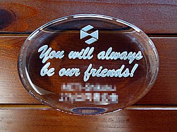 「会社のマーク、You will always be our friends、○○様」を彫刻した、定年退職のお祝い品用のガラス製ペーパーウェイト