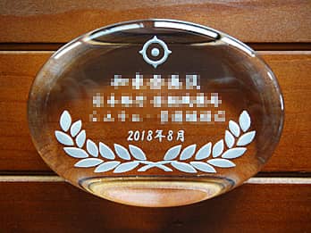「会社のマーク、表彰内容、受賞者の名前、贈呈日の日付」を彫刻した、表彰記念品用のガラス製ペーパーウェイト