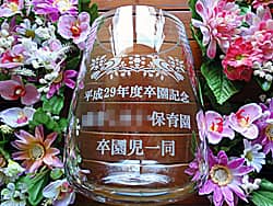 「卒園記念、○○保育園、卒園児一同より」を側面に彫刻した、保育園に寄贈するガラス花器