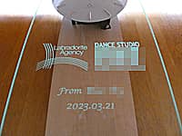 「ダンススタジオのロゴマーク、贈り主の名前、開業日の日付」を前面ガラスに彫刻した、ダンススタジオの開業祝い用の振り子型掛け時計