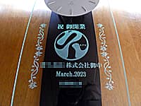「祝 御開業、贈り先のロゴマークと会社名、開業日の日付、贈り主の名前」を前面ガラスに彫刻した、開業祝い用の壁掛け時計