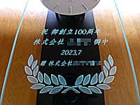 「祝 御創立100周年、会社名、日付、贈り主の会社名」を前面ガラスに彫刻した、会社創立100周年祝い用の壁掛け時計