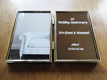 「1st Wedding Anniversary、旦那様と奥さまの名前、結婚記念日の日付」を彫刻した、結婚記念日祝い用のブック型写真立て