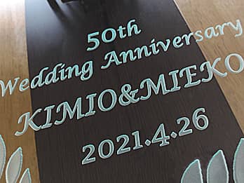 金婚式のお祝い品用の掛け時計の前面ガラスに彫刻した、「お祝いメッセージ（50th Wedding Anniversary）、旦那様と奥さまの名前、日付」のクローズアップ画像