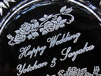 結婚祝い用のガラス製灰皿の底面に彫刻した、「Happy Wedding、新郎と新婦の名前」のクローズアップ画像